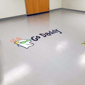 Go Daddy logo painted on a gray hallway floor near a wooden door.