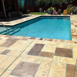 Backyard swimming pool with blue water and a tan stone patio