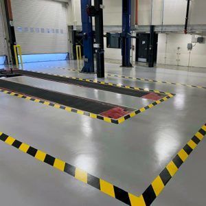 Empty vehicle service bay with yellow-black hazard markings and car lifts in a clean garage