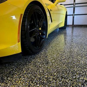 Yellow sports car with black wheels parked in a garage on a speckled epoxy floor