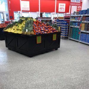 Supermarket produce display with assorted fruits and vegetables on a black island, surrounded by aisles and sale signs