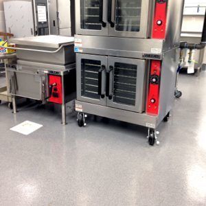 Commercial kitchen with stainless steel ovens and prep table on a gray floor