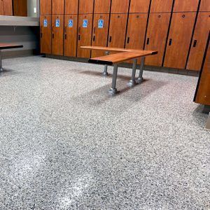 Lockers in a school hallway with a wooden bench and speckled floor.