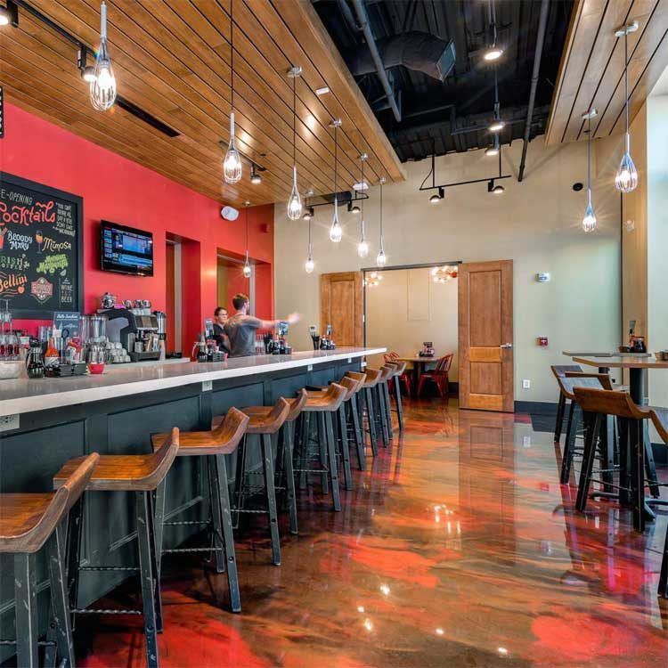 Empty modern bar with wooden stools, red accent wall, and glossy floor under pendant lights
