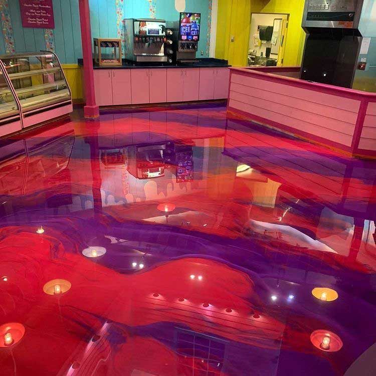 Vibrant indoor café with a glossy pink-red floor, counter seating, and a refrigerated display case.