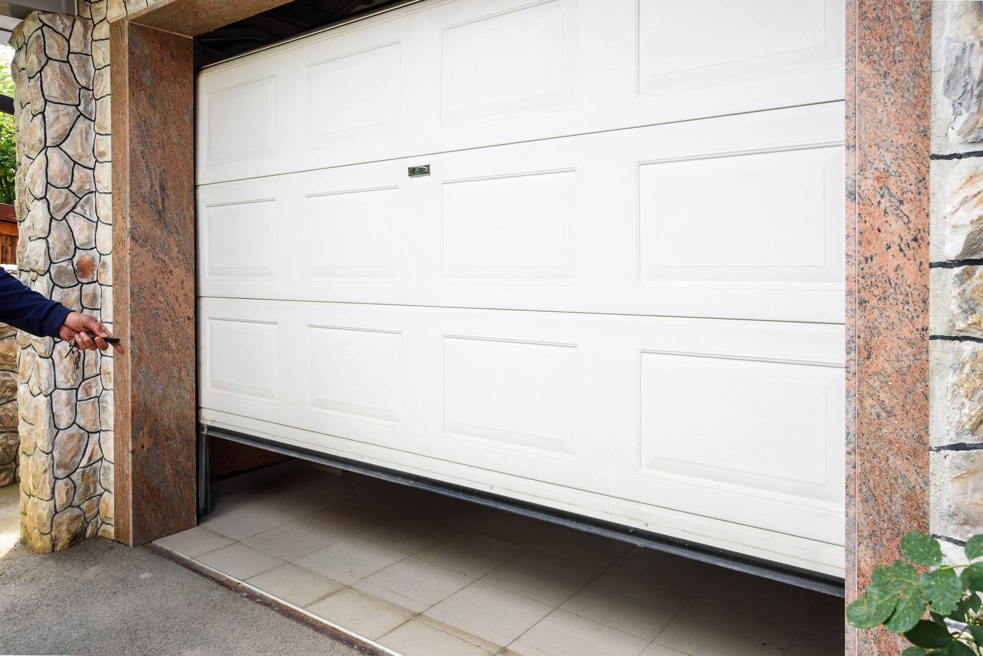 White garage door partially open in a stone-framed driveway entrance