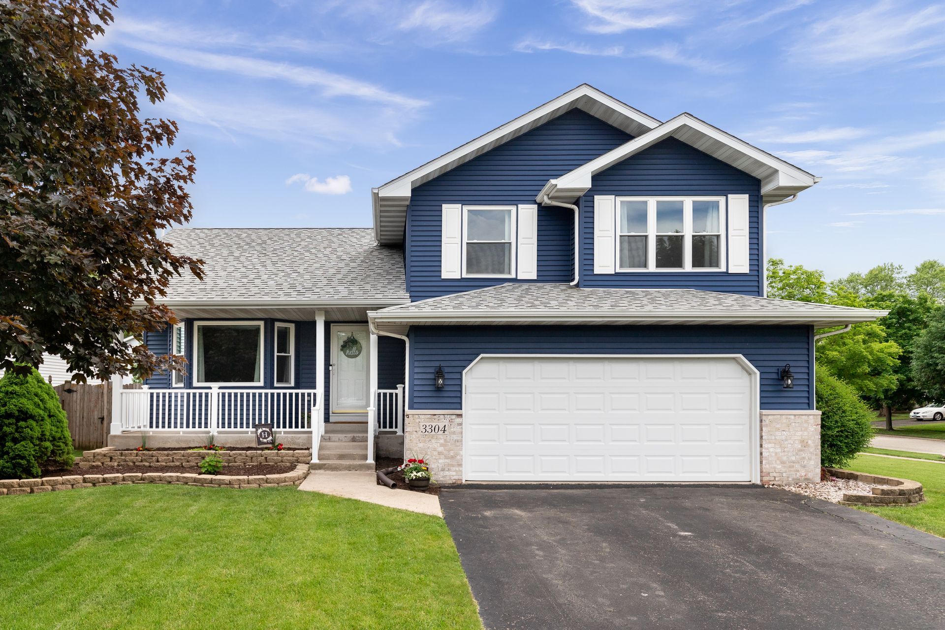 Blue two-story suburban house with white trim, attached garage, and green lawn under a clear sky