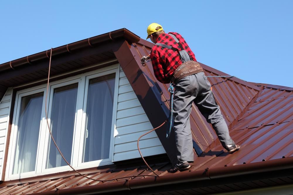 A Man Is Working on The Roof of A House — Apex Roofing Group in Brunswick Heads, NSW