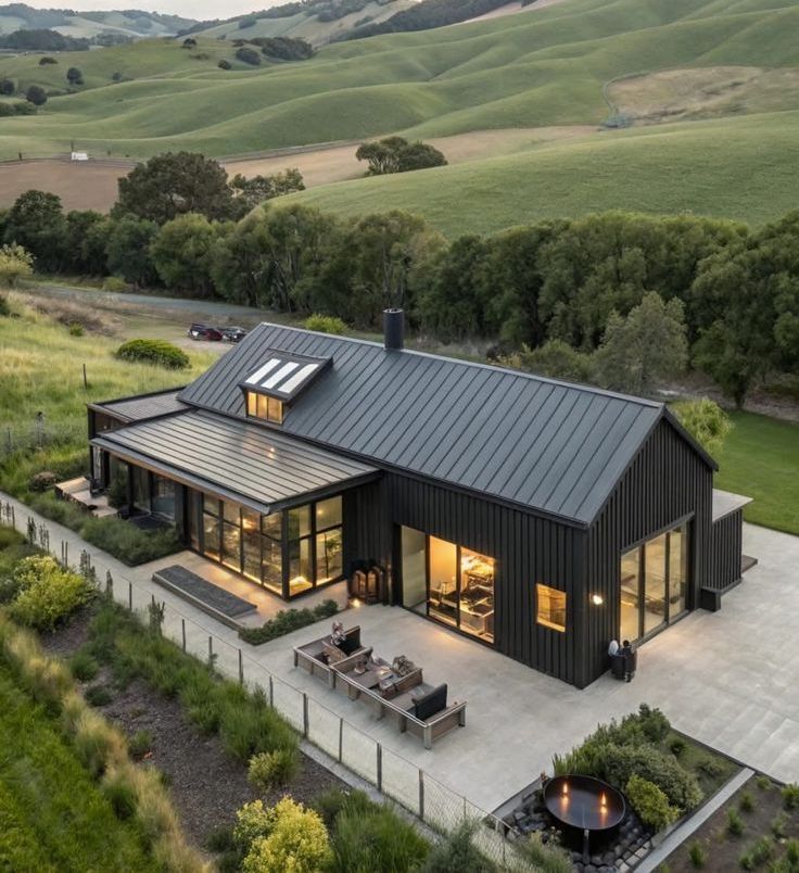 Modern black farmhouse-style home with a standing seam metal roof, large glass windows, and outdoor entertainment areas, nestled in rolling green countryside — Apex Roofing Group in Byron Bay, NSW