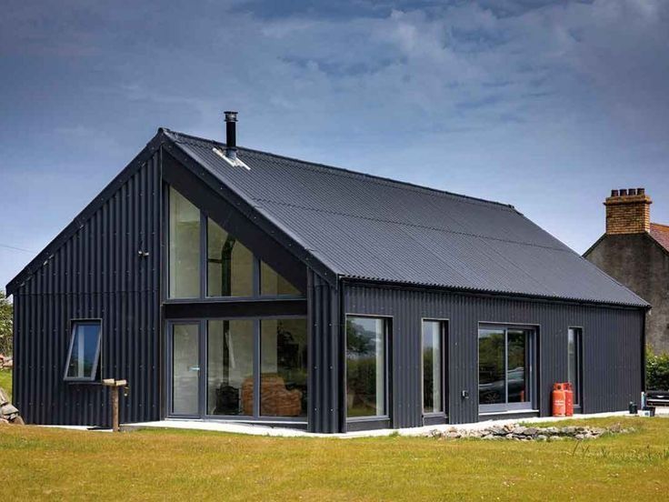 Modern black-clad house with a pitched corrugated metal roof and large floor-to-ceiling windows, set in a rural landscape under a moody sky. — Apex Roofing Group in Byron Bay, NSW