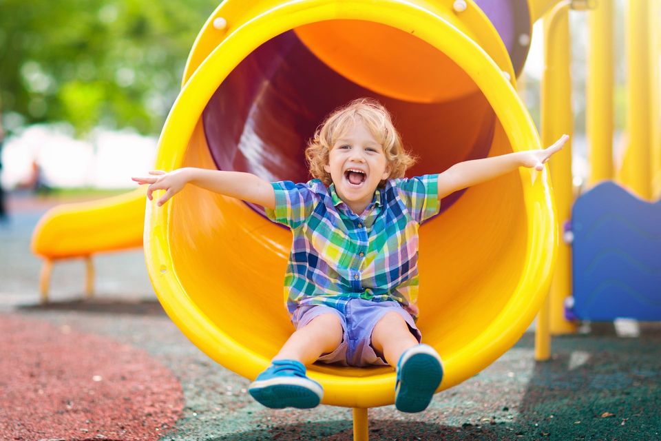 Smiling child sitting at the mouth of a yellow playground slide with arms outstretched