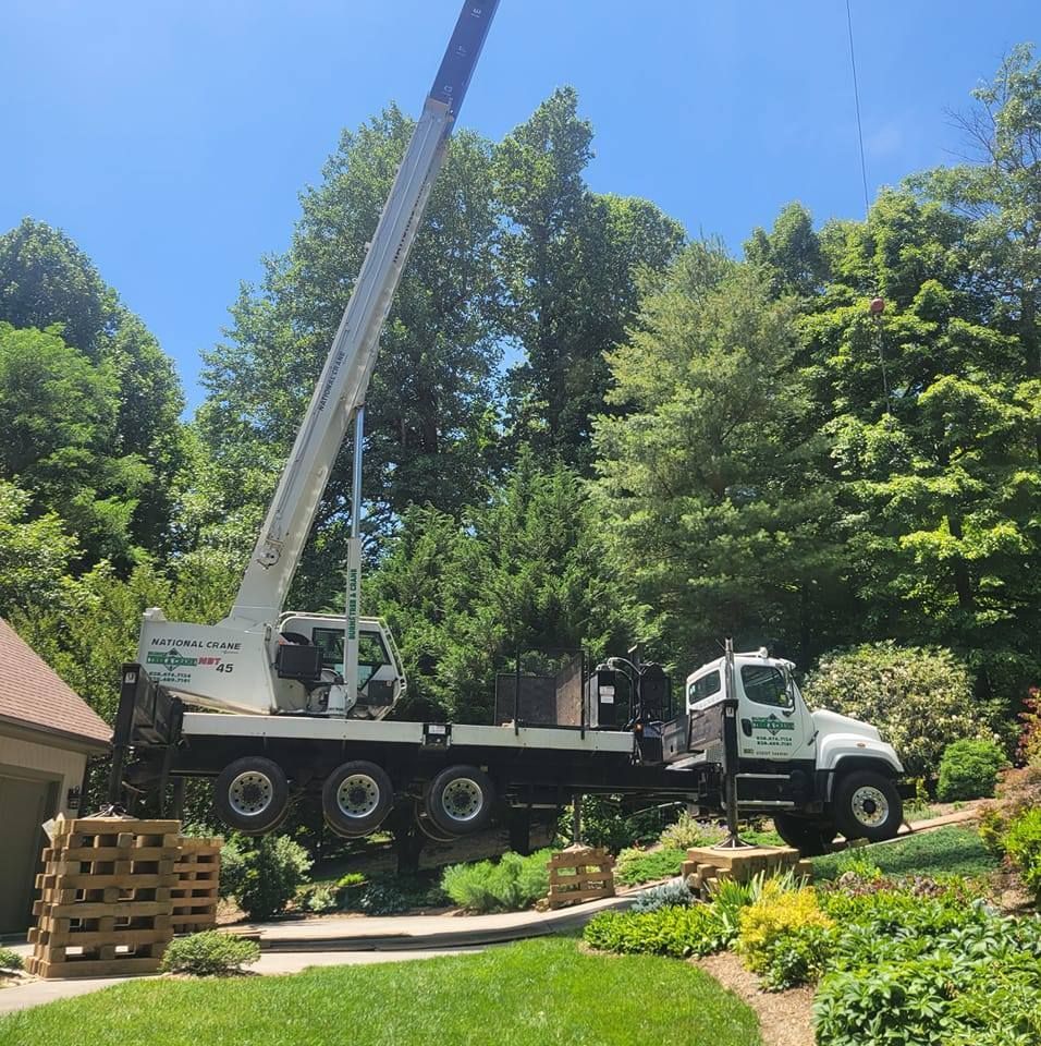 A large white crane truck lifting materials in a residential yard with greenery.