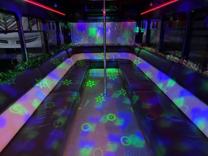 Empty party bus interior with glowing green and purple disco lights on benches and floor