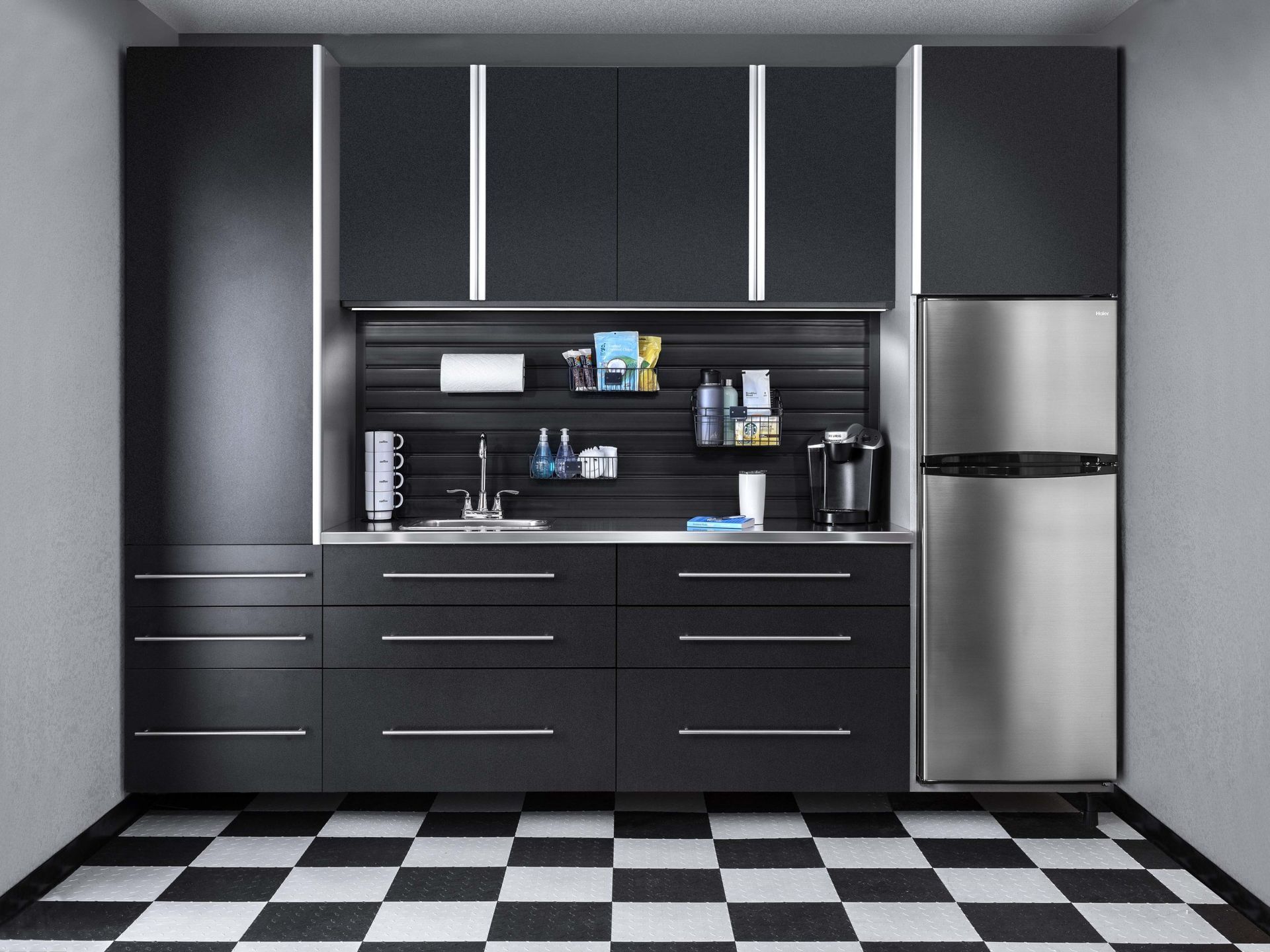 A modern kitchenette with matte black cabinets, stainless steel appliances, and a black-and-white checkered floor.