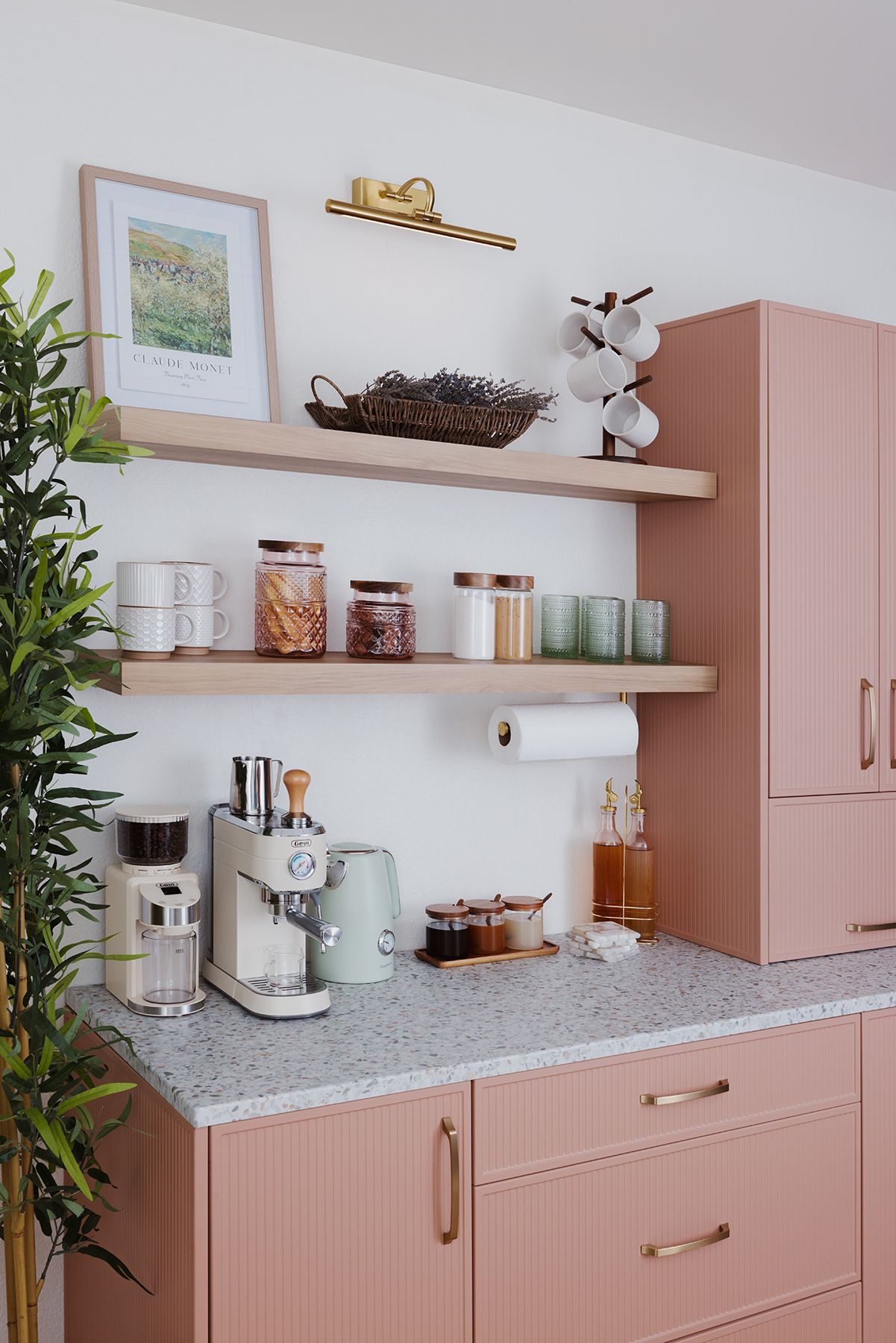 Pink kitchen bar cabinets with open shelves, small appliances, jars, and a speckled countertop against a white wall