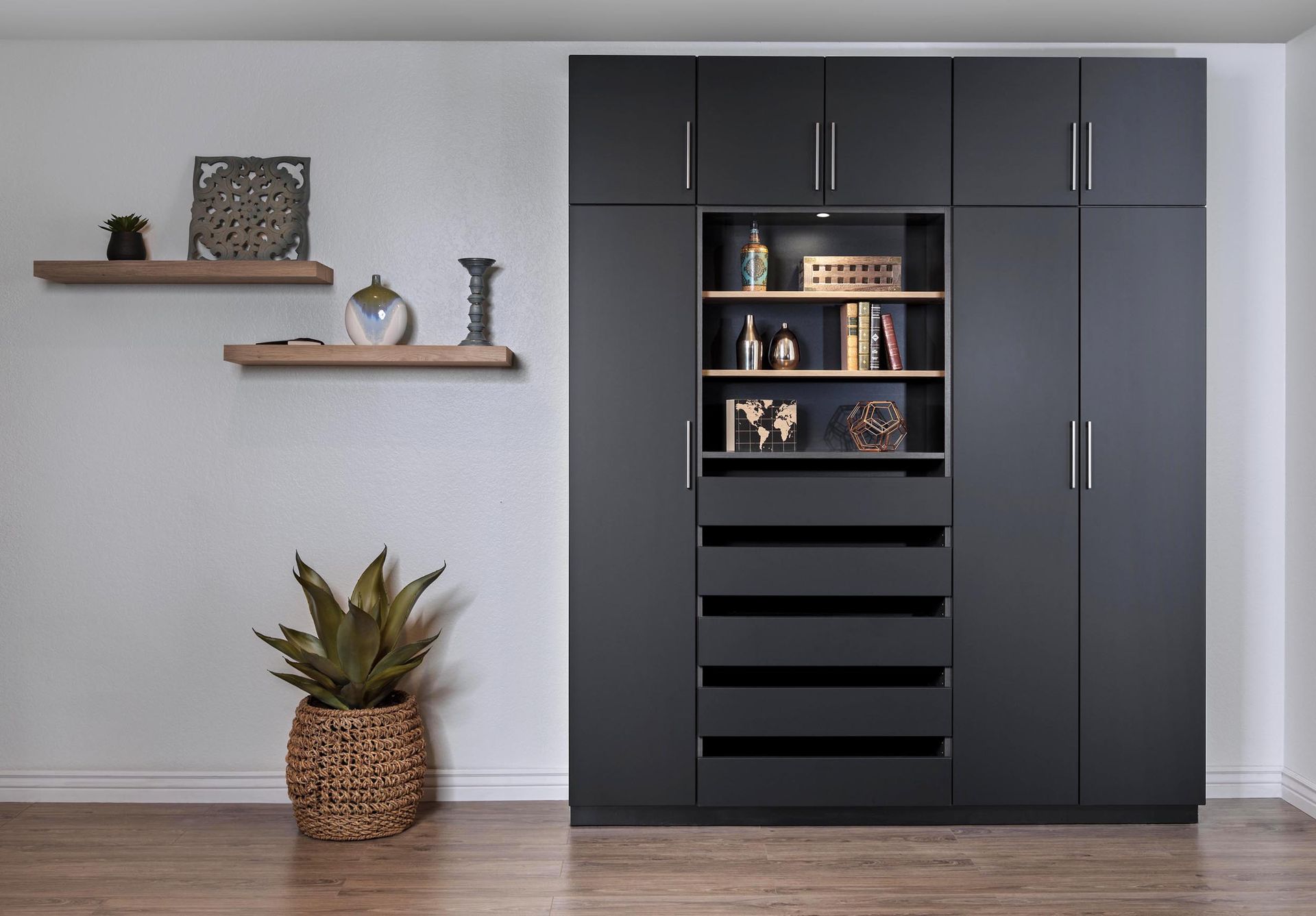 Modern dark-gray cabinet with open shelves and drawers in a minimalist room with wall shelves and a potted plant