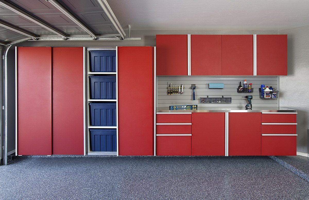 Red garage cabinets with overhead storage, a slatwall, and a workbench area against a gray wall in a garage.