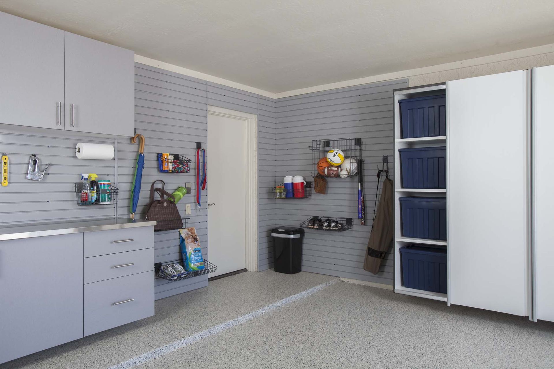 Organized garage with cabinets, hanging tools, cleaning supplies, and a white storage closet