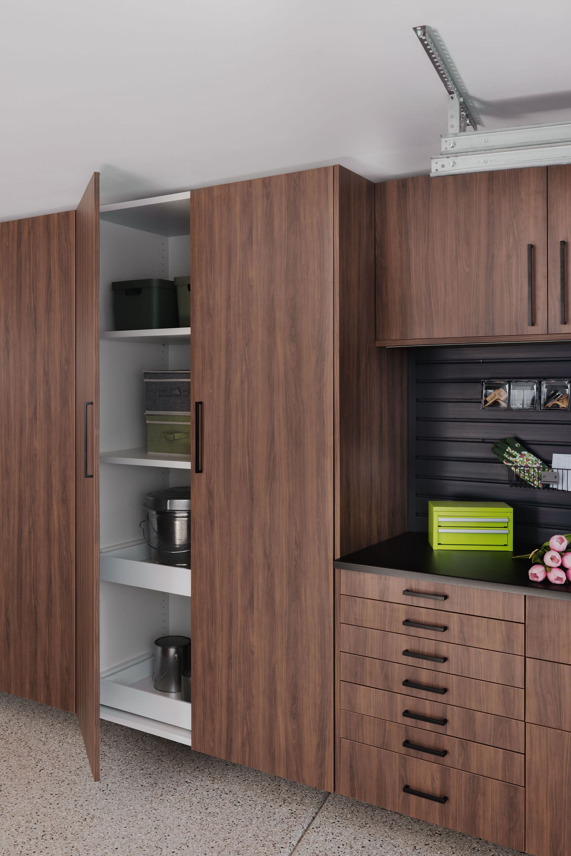 Modern wood-grain garage cabinets with pull-out shelves, a black slat wall, and stacked drawers on a speckled floor.