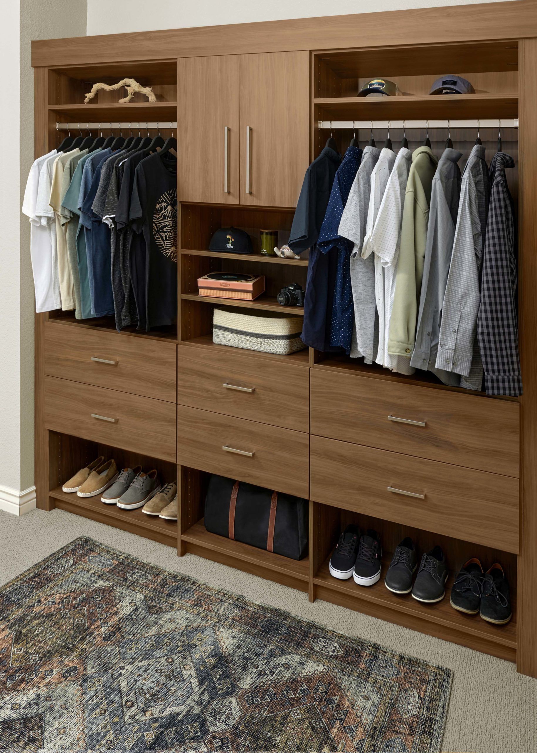 Wooden built-in closet with hanging clothes, drawers, shelves, and shoes on a patterned rug.