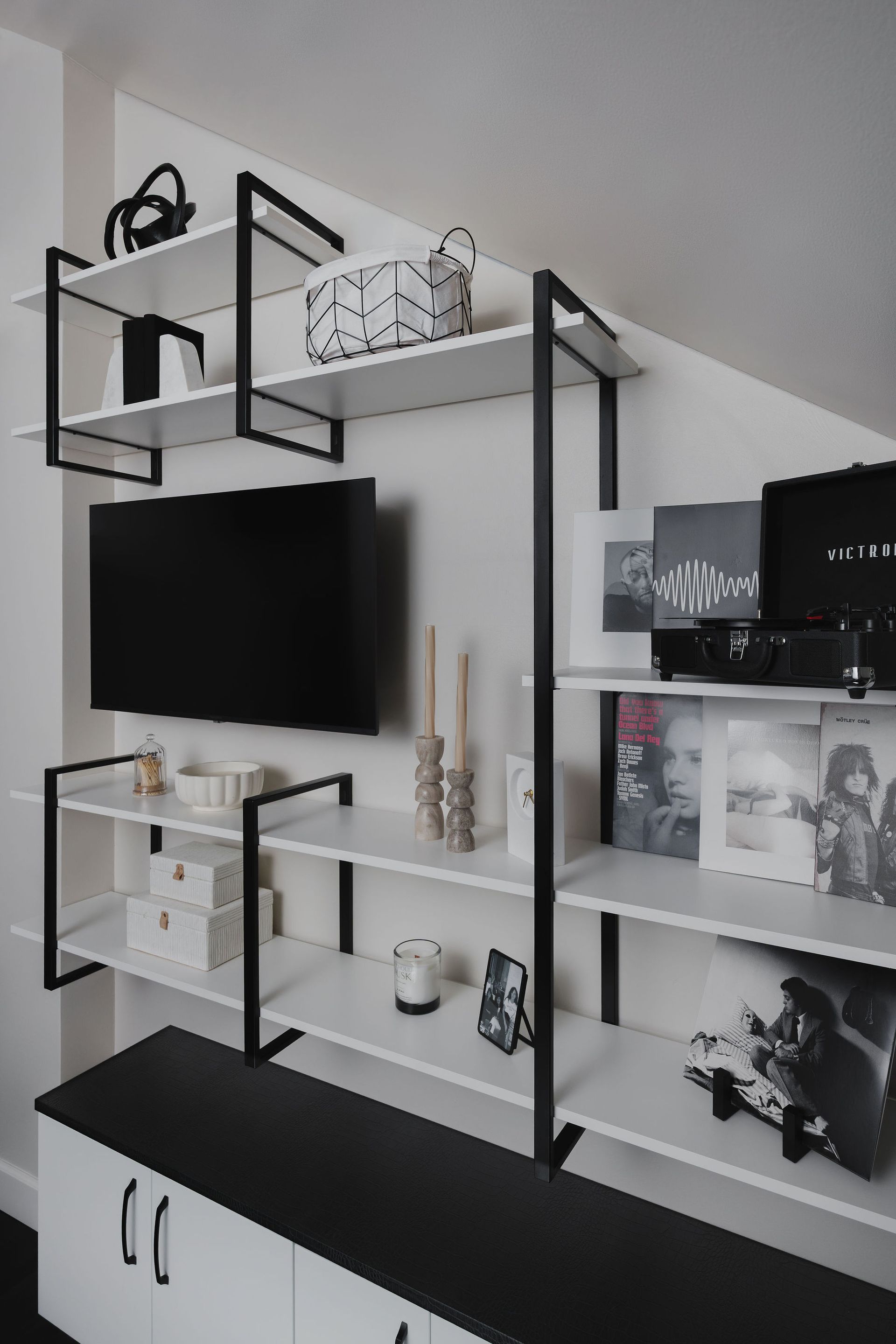 Black and white wall-mounted shelving unit with a TV and decorative display items in a modern room