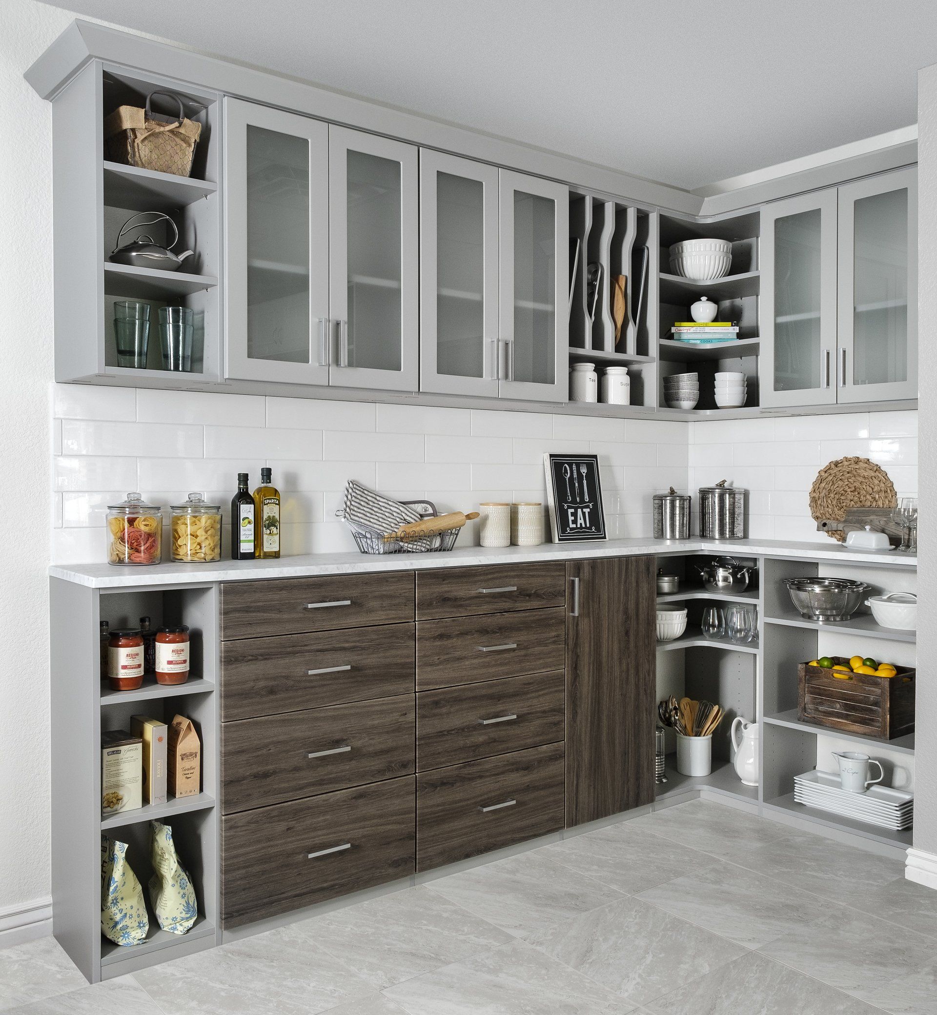 Modern kitchen with gray cabinets, dark wood drawers, open shelving, and pantry items on white countertops