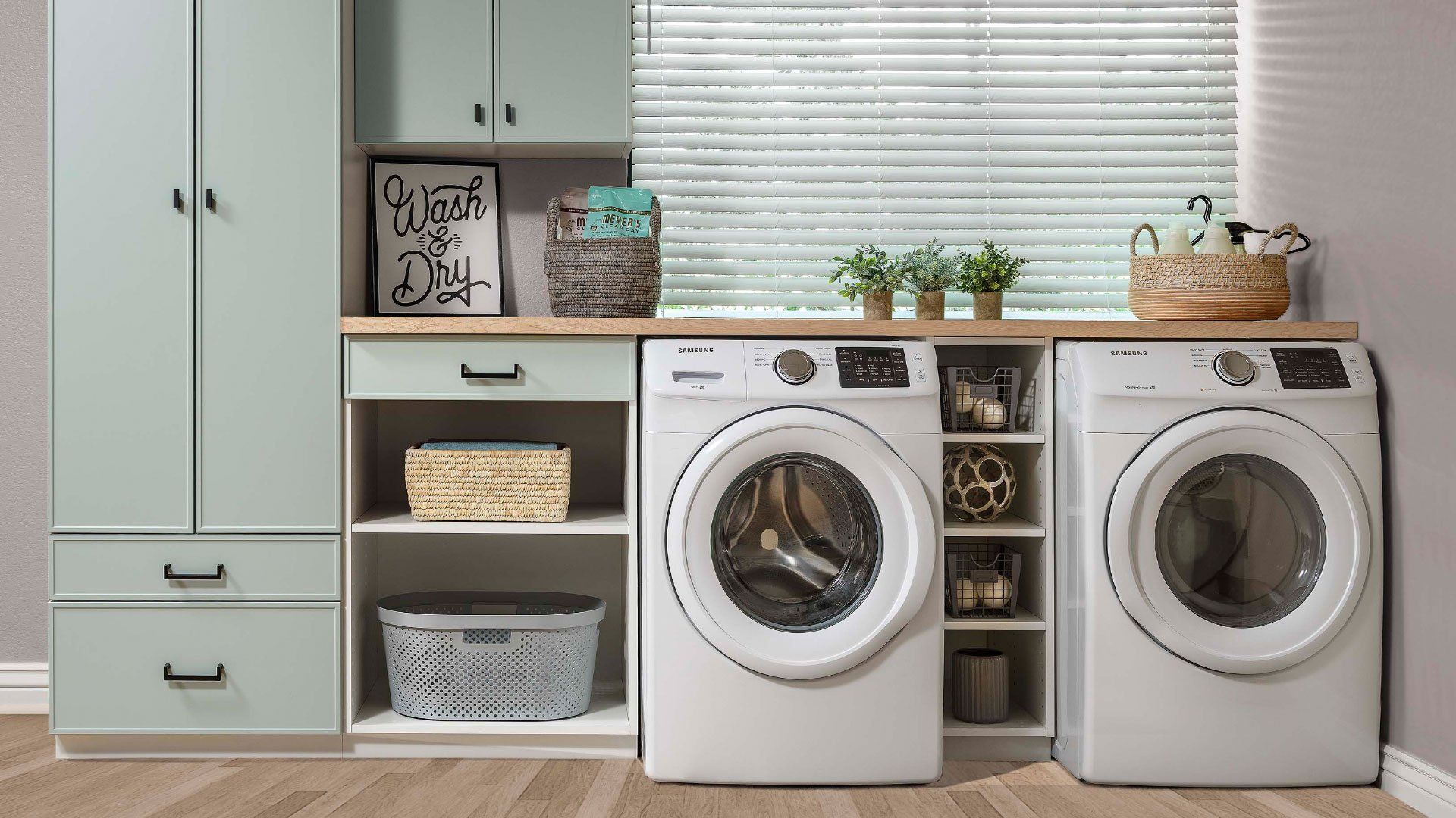 Modern laundry room with washer and dryer, pale green cabinets, shelves, and wicker baskets
