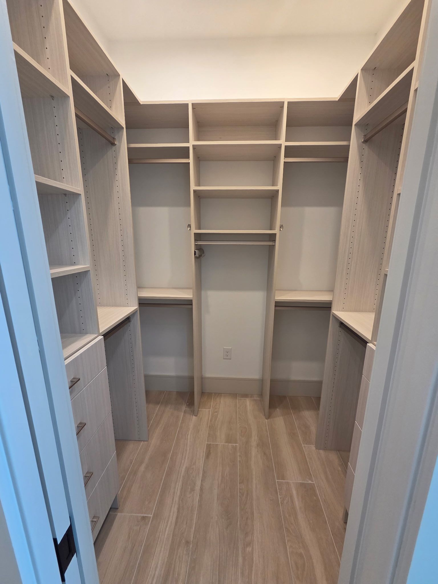 Walk-in closet with built-in beige shelves, drawers, and hanging rods, viewed from the doorway.