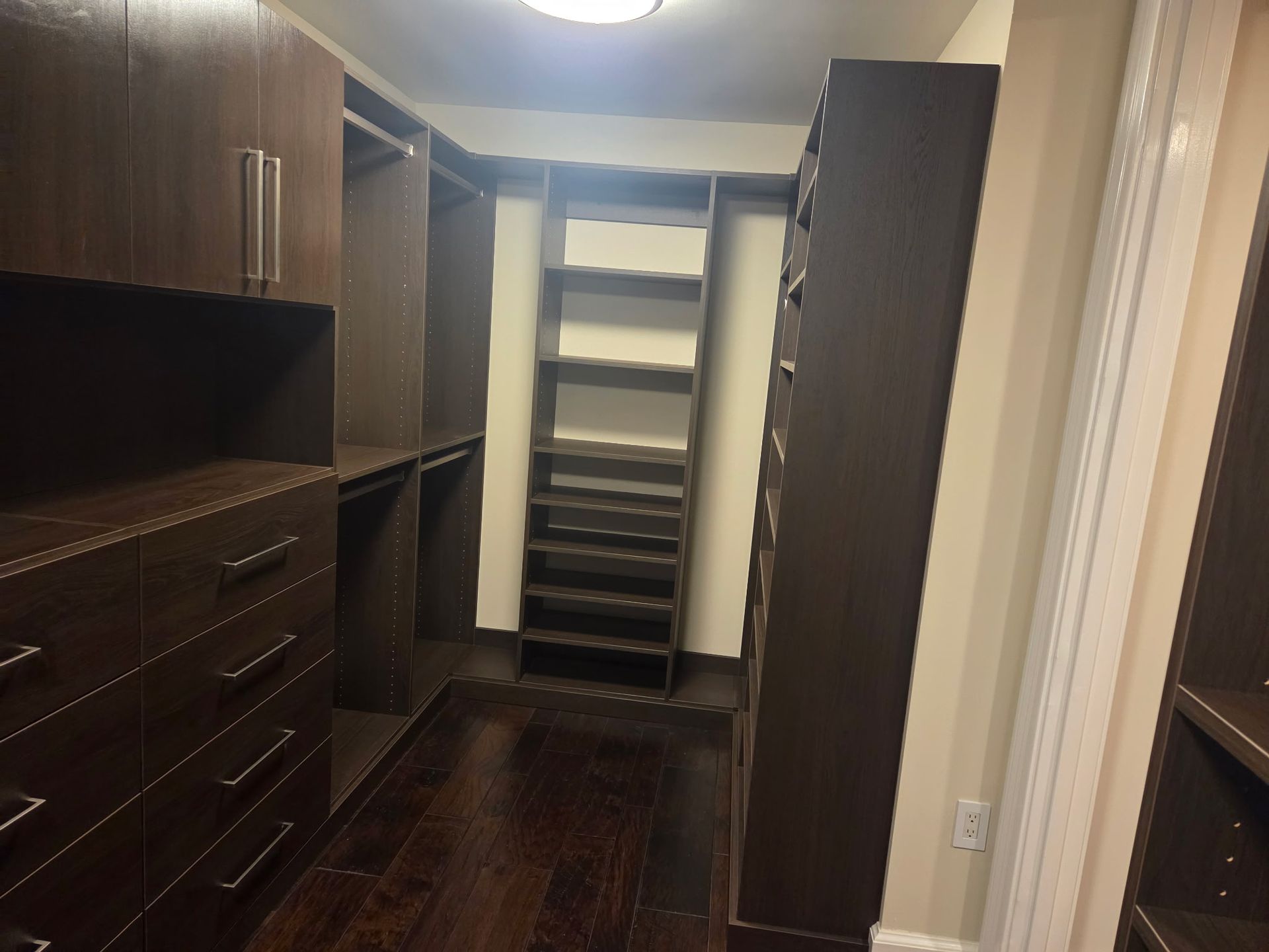 Walk-in closet with dark wood shelves, drawers, hanging rods, and an empty center aisle