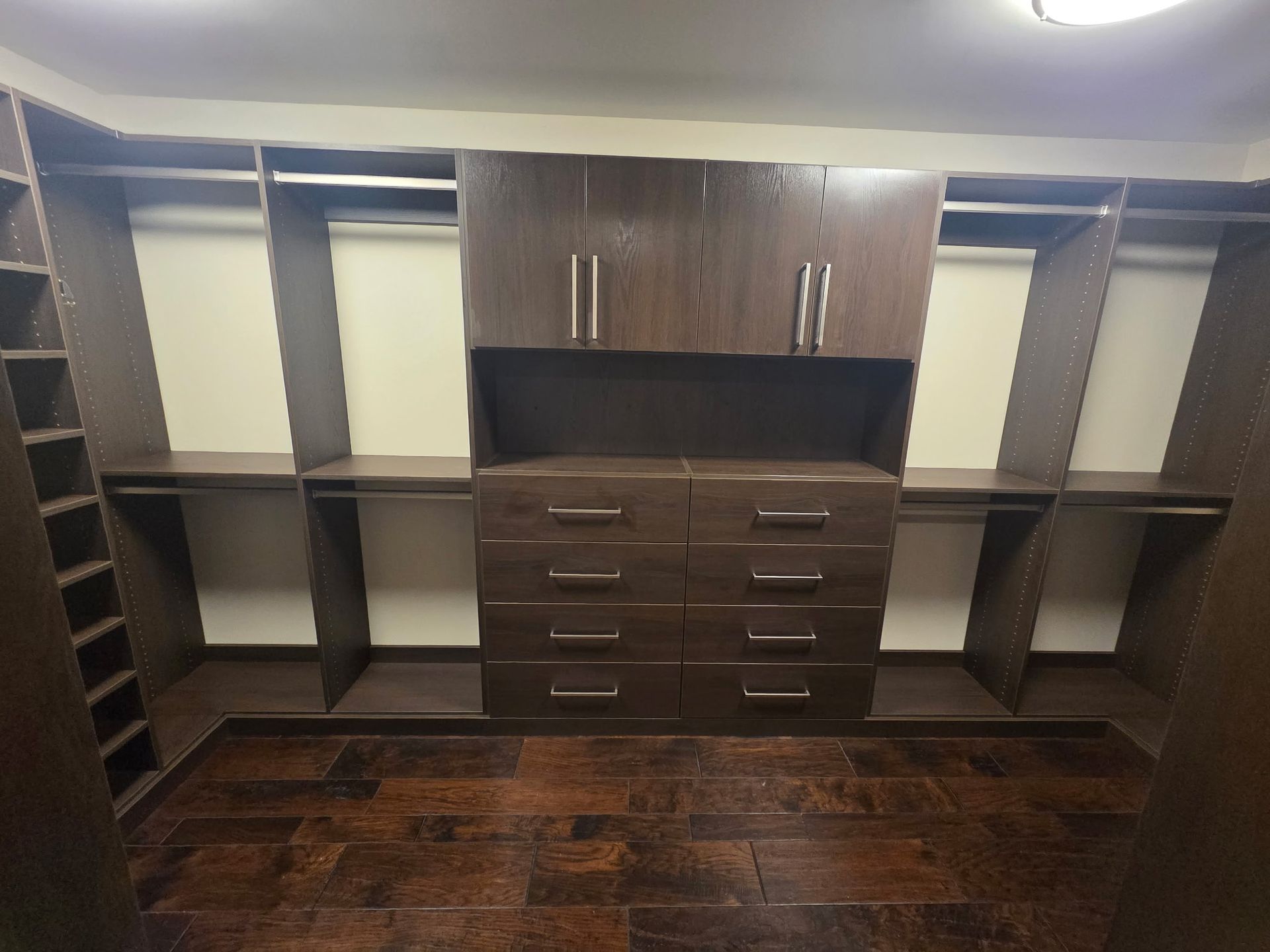 Walk-in closet with dark wood shelves, drawers, and hanging rods on wood flooring