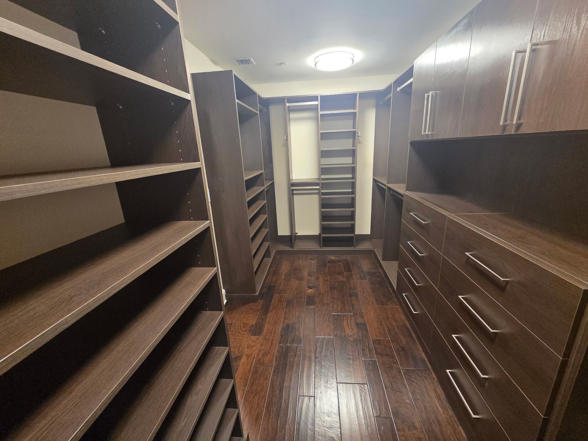 Walk-in closet with dark wood shelves, drawers, and hanging rods, viewed from the doorway