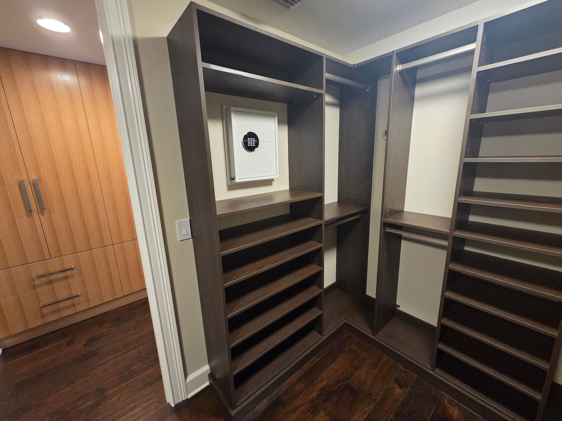 Walk-in closet with dark wood shelving, hanging space, and built-in drawers on the left.