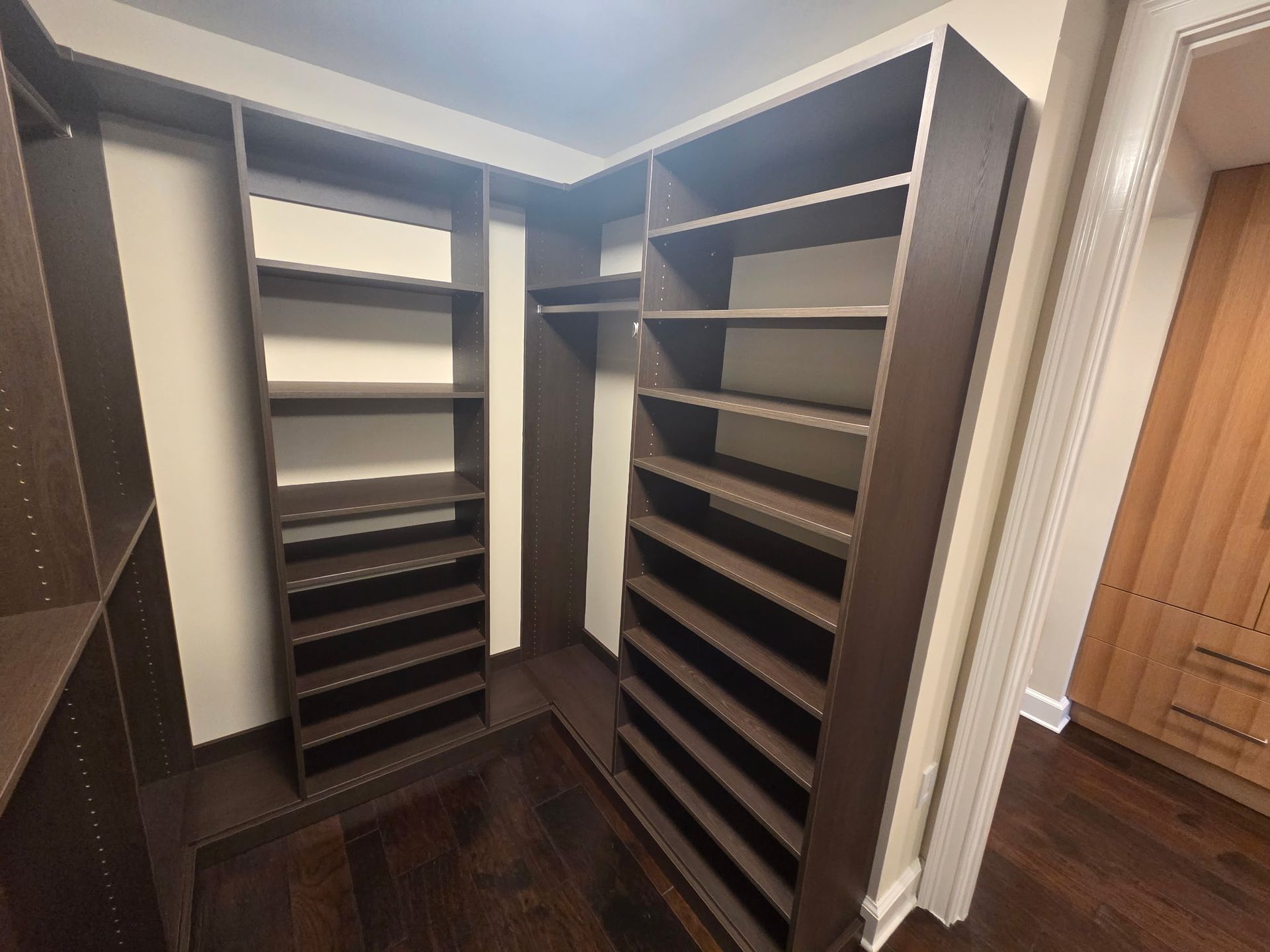 Open walk-in closet with dark wood shelving and hanging rails, lit by recessed ceiling lights.