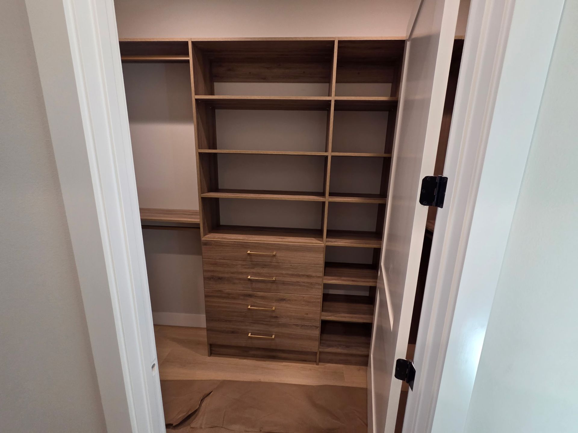 Open closet with built-in wooden shelves and drawers, viewed through white double doors.