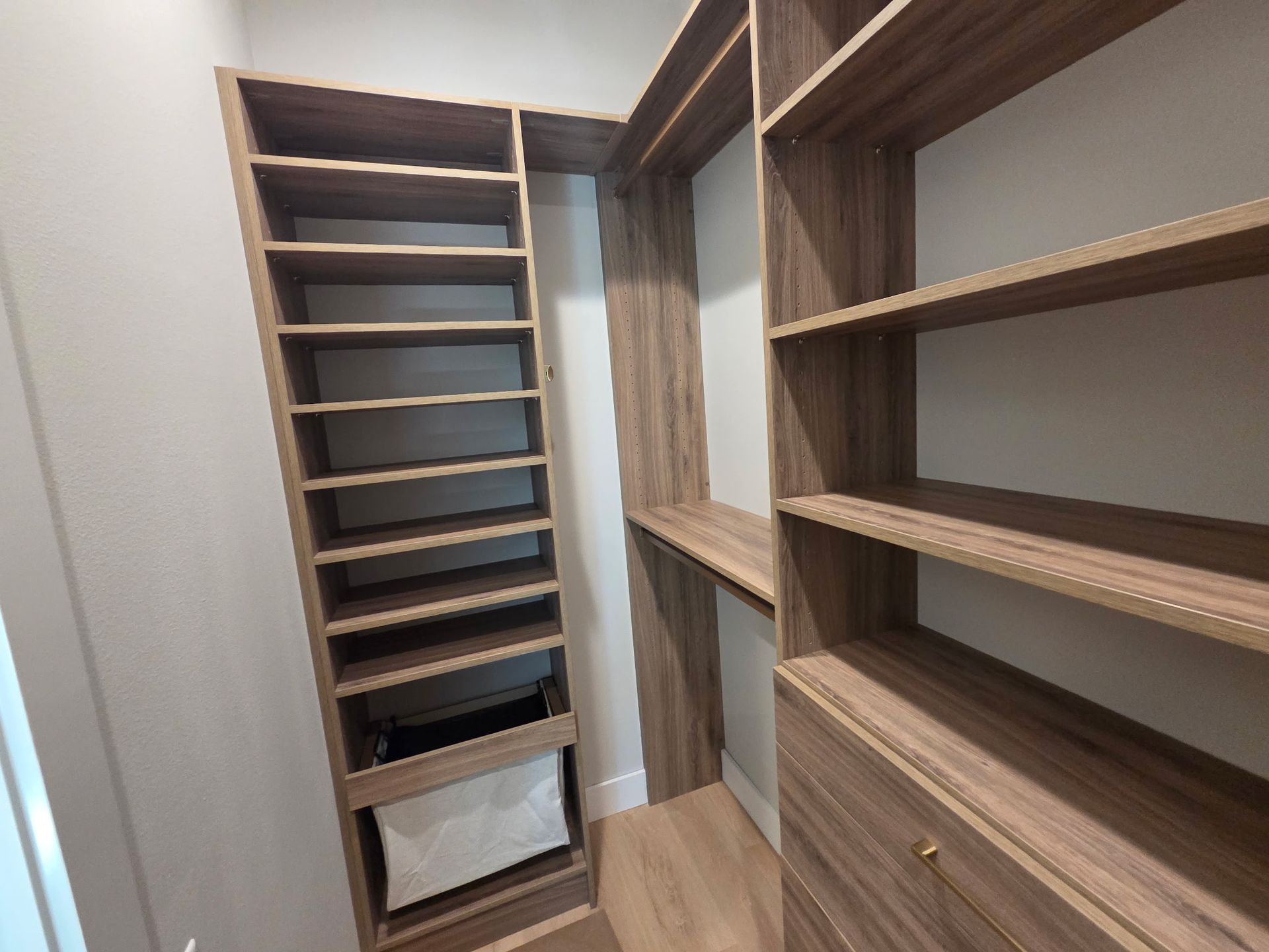 Empty walk-in closet with dark wood shelving and drawers, viewed down a narrow aisle.
