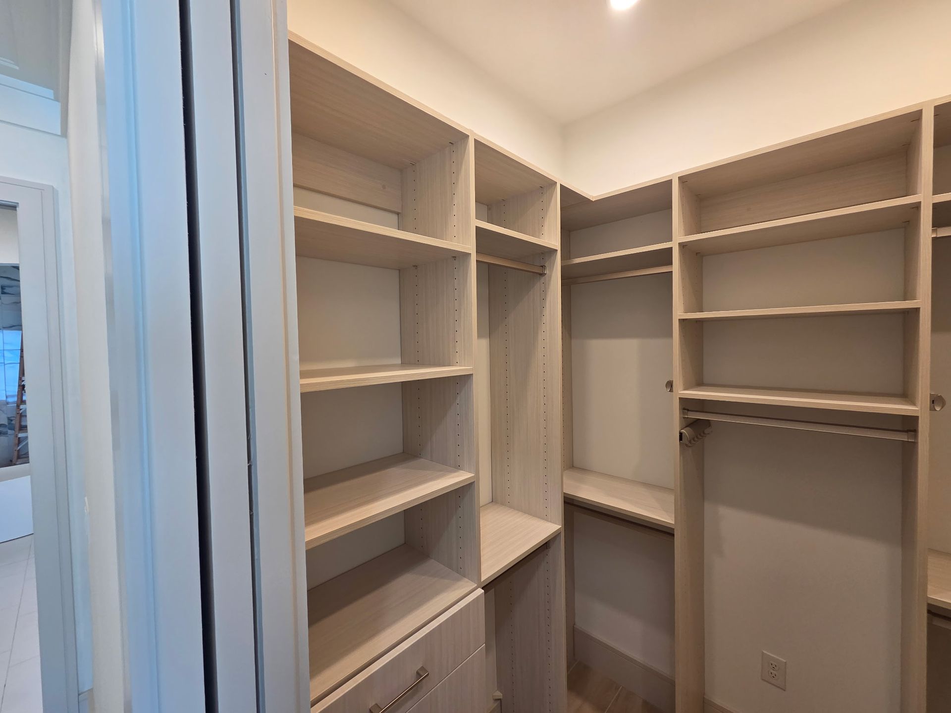 Built-in white walk-in closet with shelves, hanging rods, and drawers in a bright room