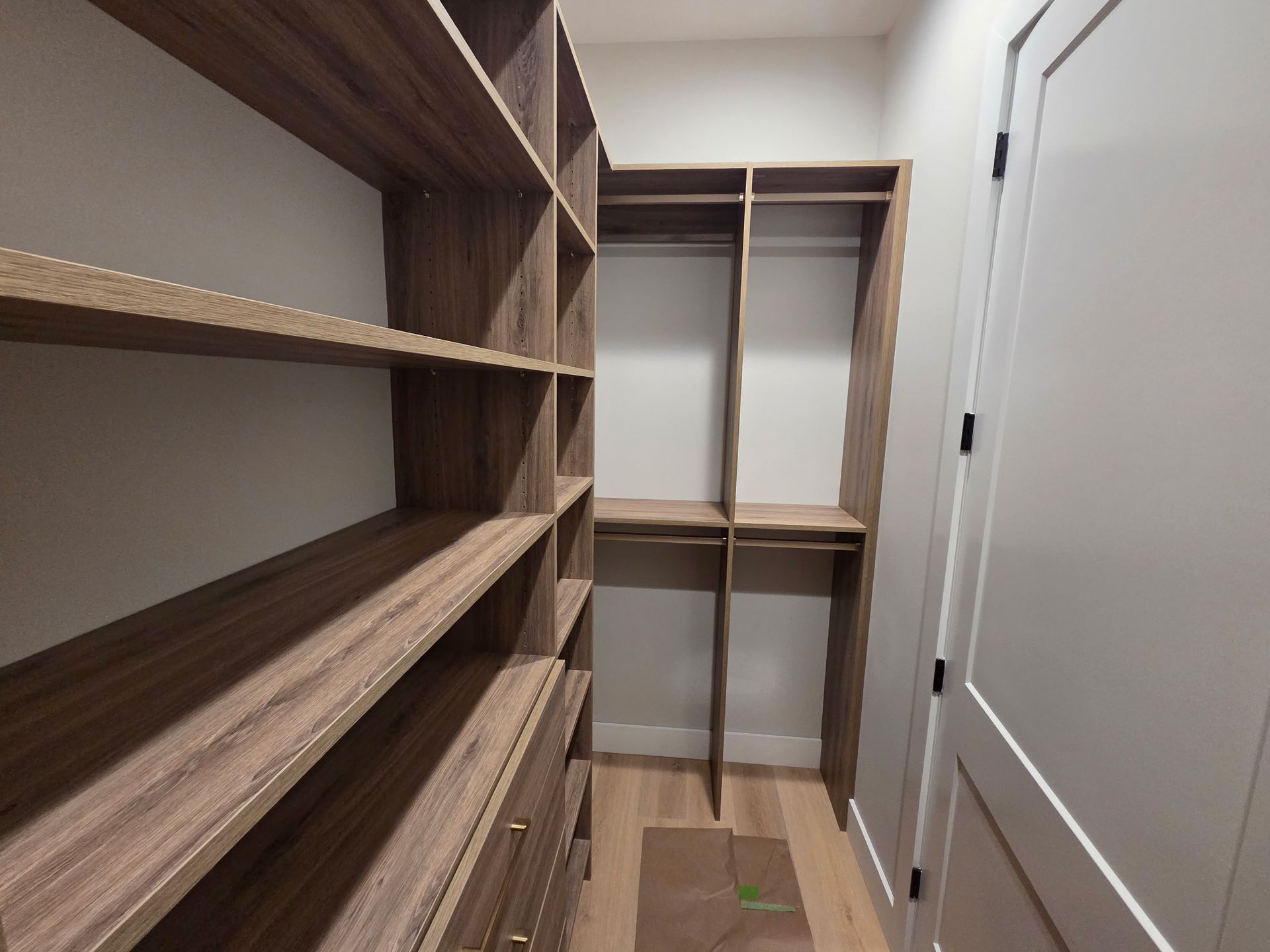 Walk-in closet with empty wooden shelves, hanging rods, and a doorway on the right
