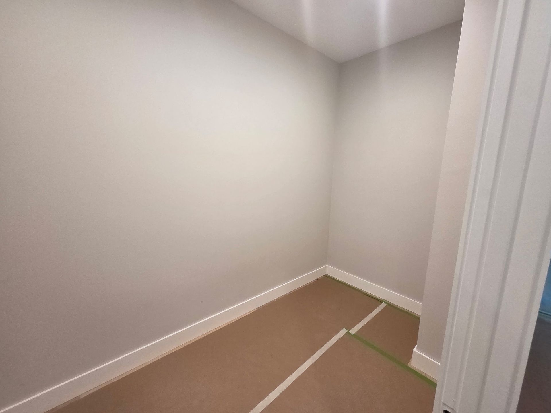 Empty carpeted corner of a white room with baseboards and green tape on the floor