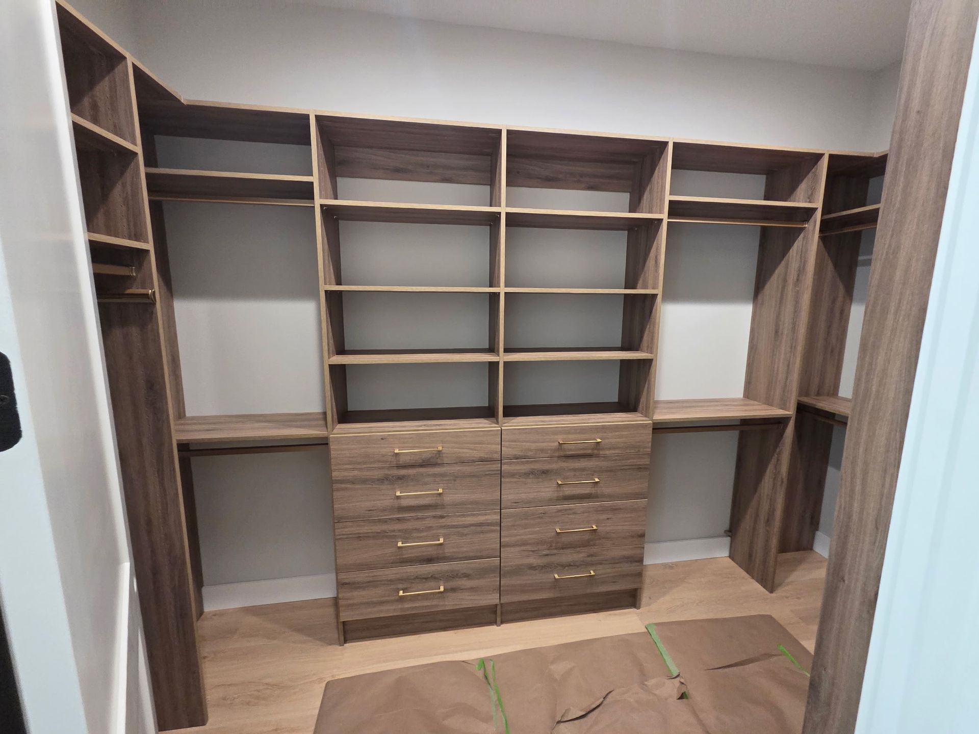 Built-in wooden closet with shelves, drawers, and hanging spaces in an empty room under construction