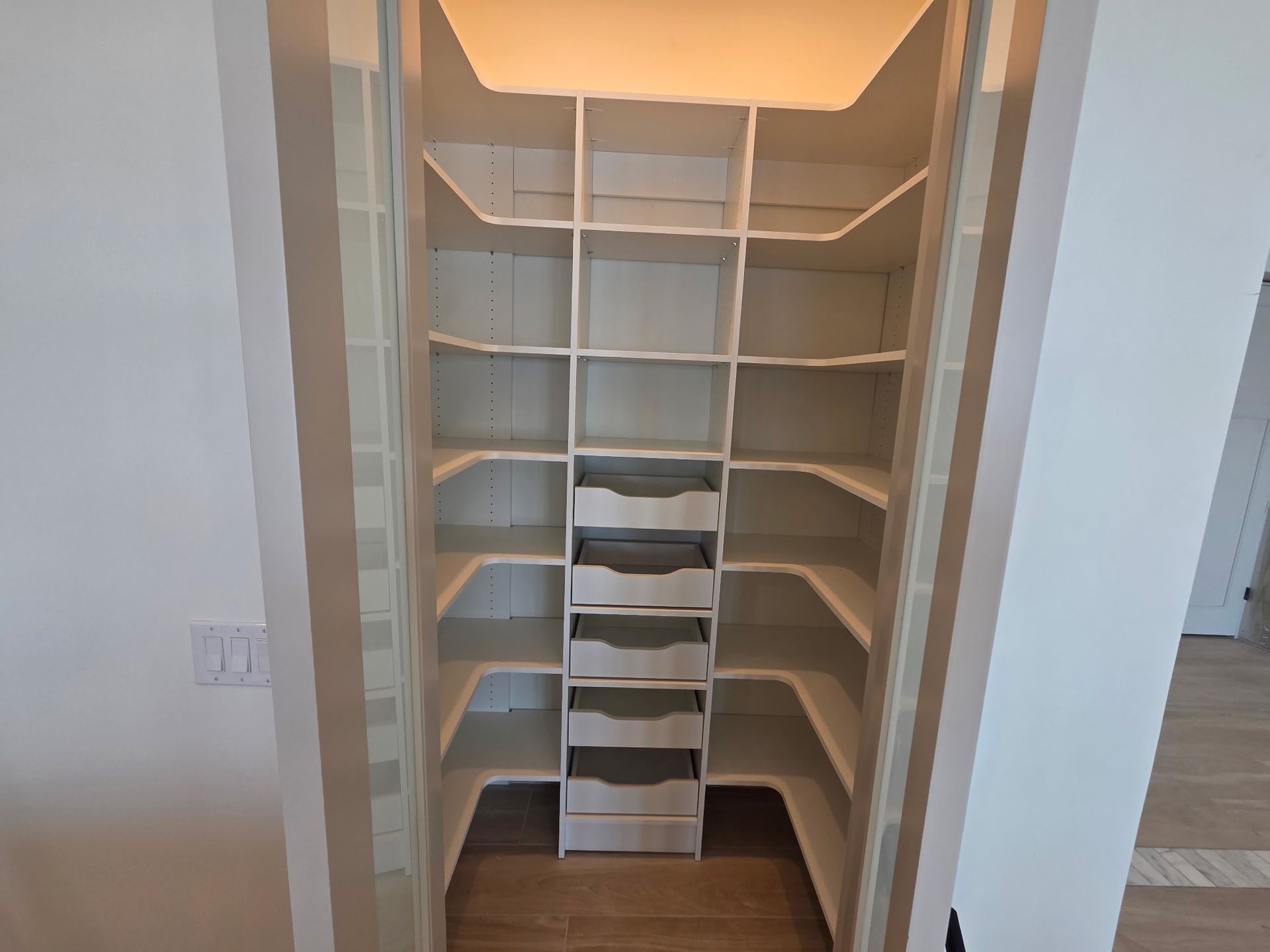 White walk-in closet with built-in shelves and drawers, lit from above