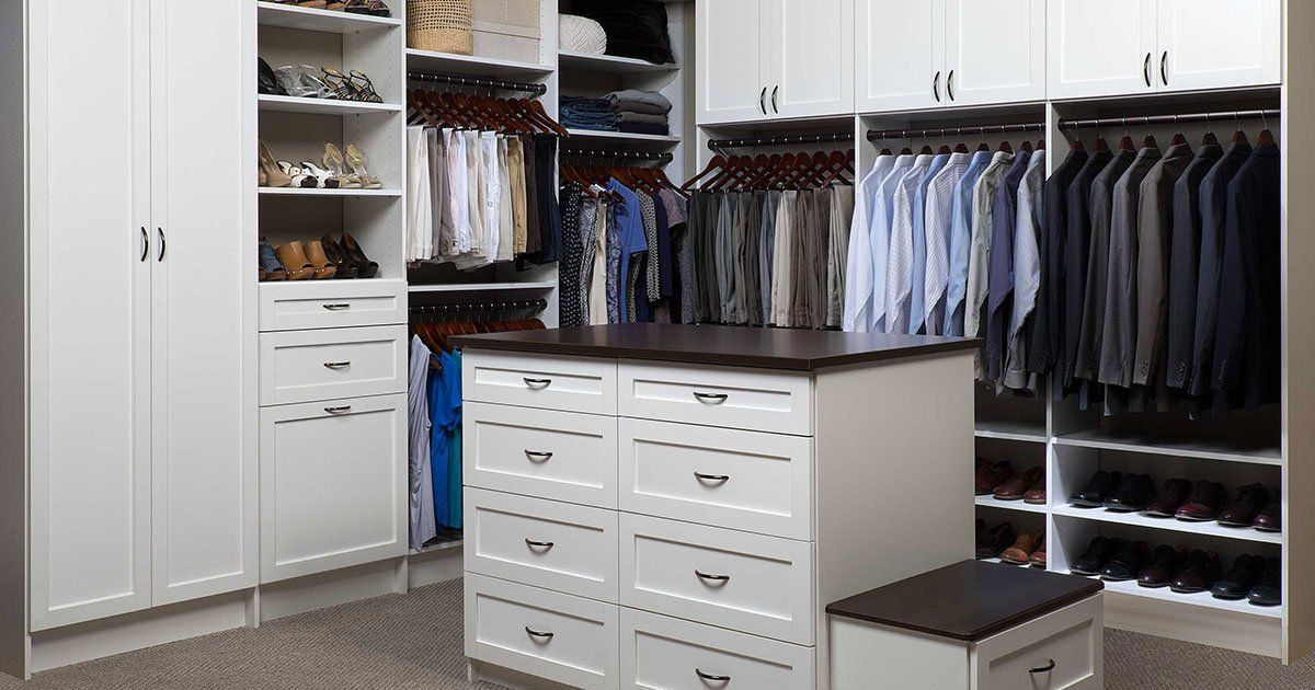 Spacious white walk-in closet with hanging clothes, shelves, drawers, and a center island storage unit