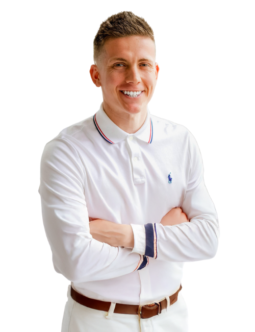 A man in a white polo shirt and white pants is standing with his arms crossed and smiling.