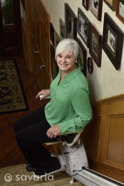 A woman in a green shirt is sitting on a stair lift.