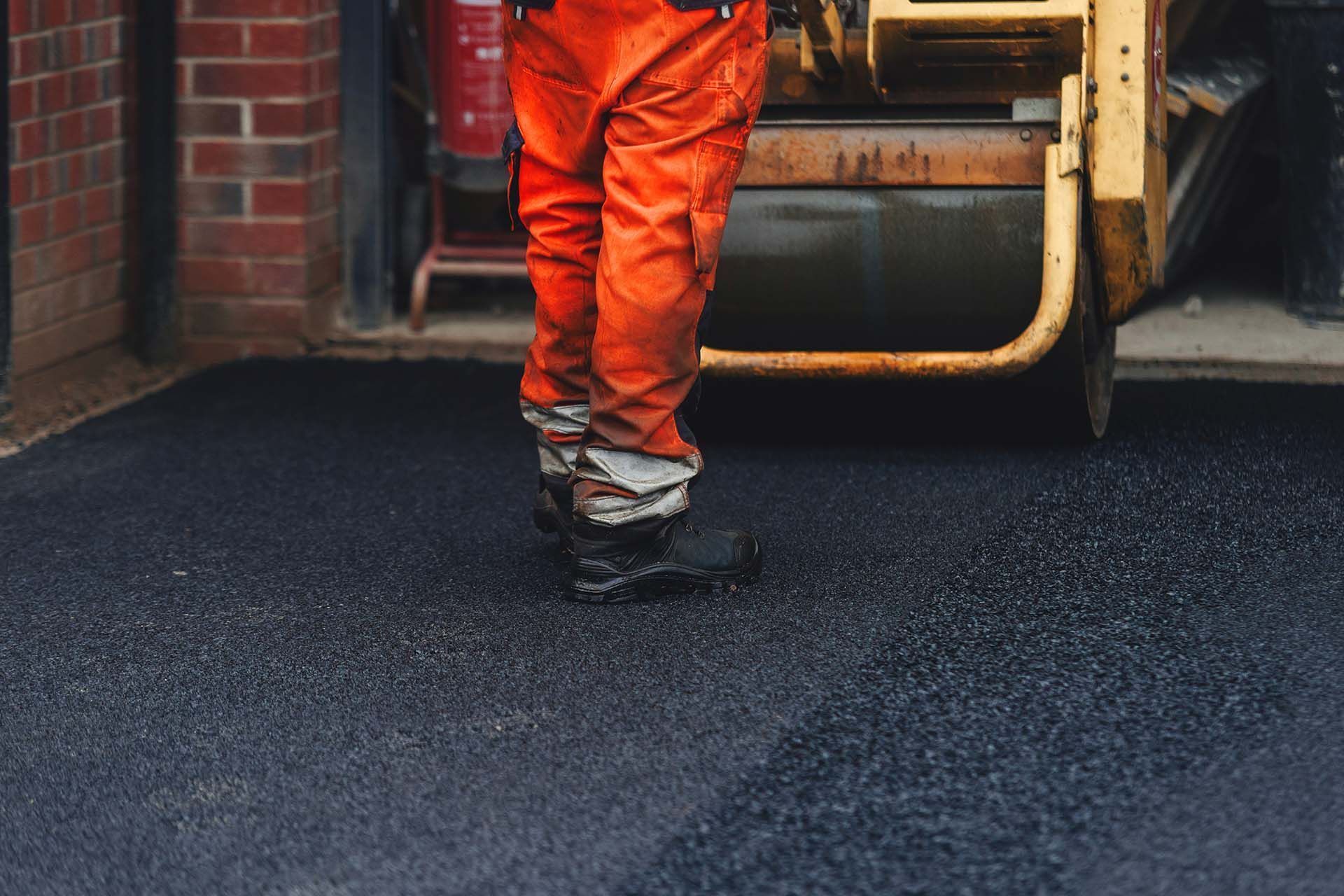 Asphalt paving contractor operating a roller on fresh pavement.