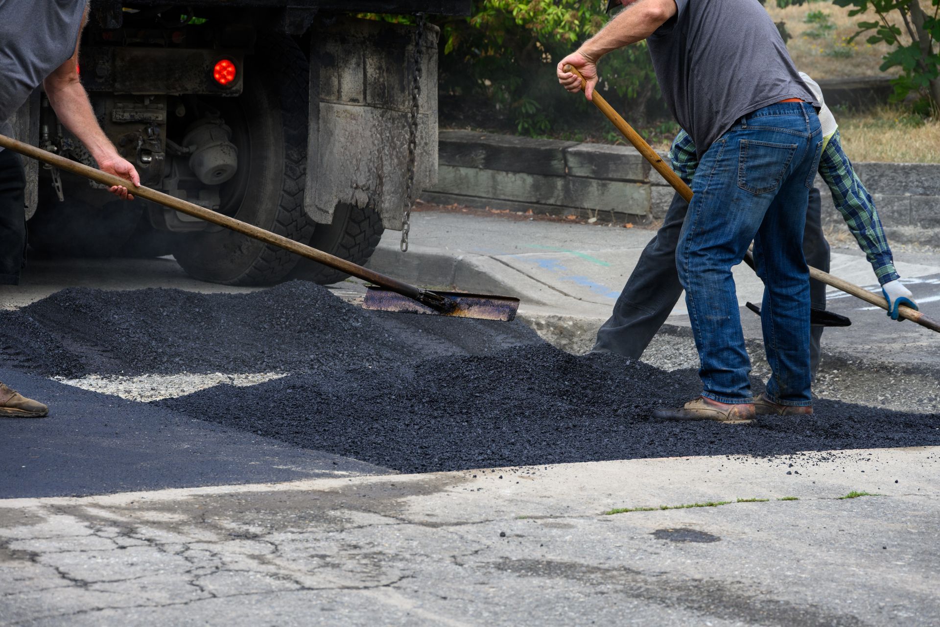 Workers from a commercial asphalt contractor spreading hot asphalt with rakes beside a dump truck Workers from a commercial asphalt contractor spreading hot asphalt with rakes beside a dump truck.