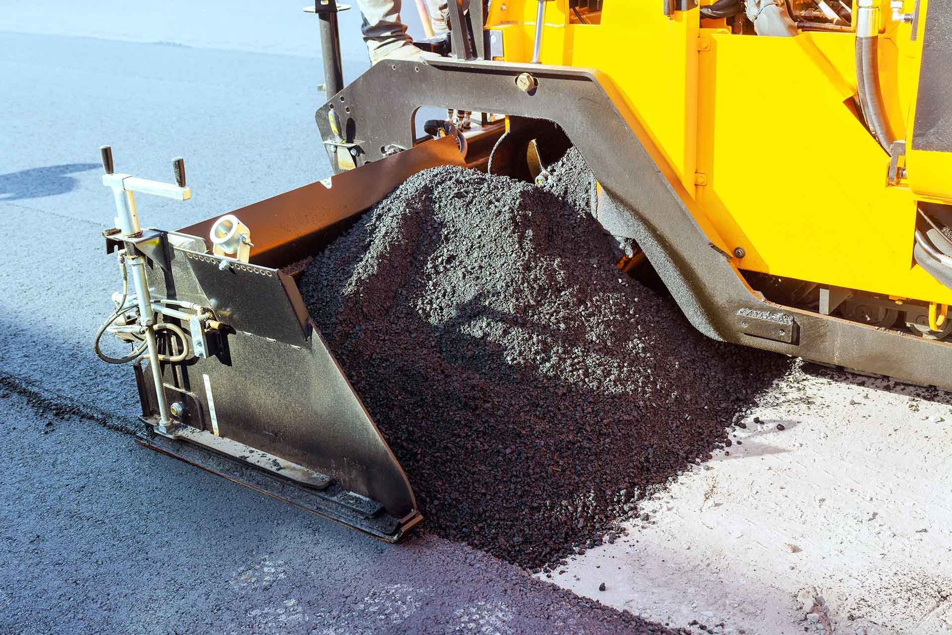 Asphalt paver spreading fresh hot mix over a roadway during paving work.
