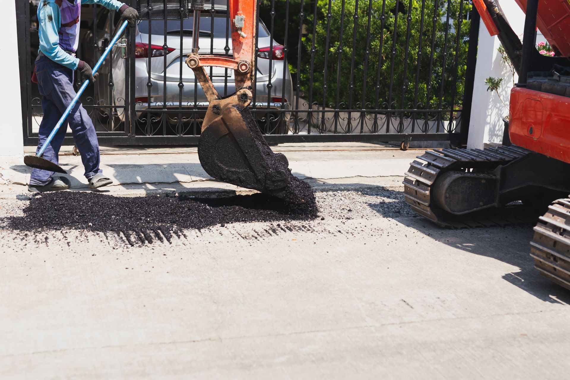 An excavator bucket pouring hot asphalt for a residential driveway repair