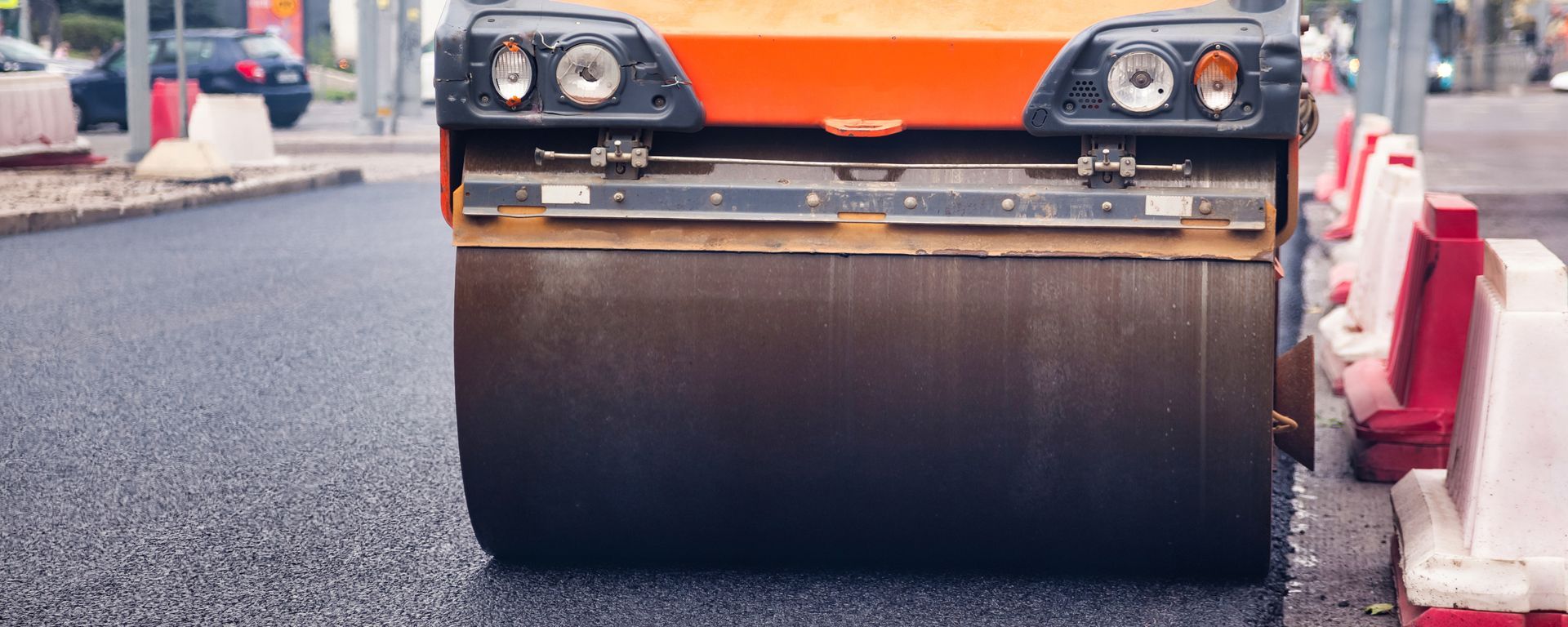 Road roller compacting fresh asphalt on a roadway beside temporary construction barriers. Road roller compacting fresh asphalt on a roadway beside temporary construction barriers.