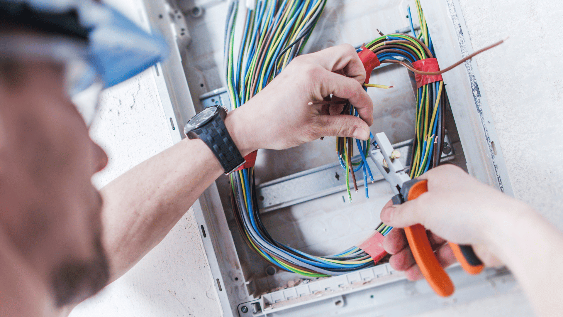 A man is working on an electrical box with a pair of pliers.