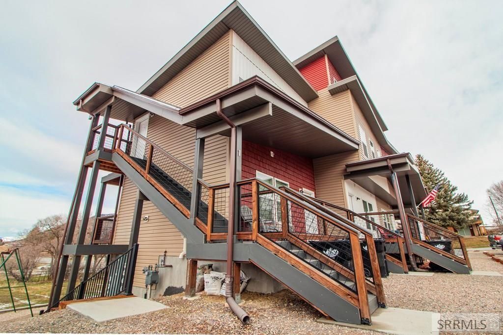 Stilted wooden house with exterior staircases and railings under a partly cloudy sky